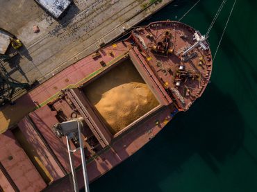 cargo ship or bulk carrier loaded to the brim with grain is preparing for departure, working sailors on deck are completing work, aerial view