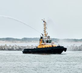 Fireboat ship sails on open sea directing jets of water to sides demonstrating bravery water salute