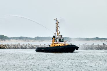 Fireboat ship sails on open sea directing jets of water to sides demonstrating bravery water salute